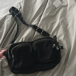 Svart axelväska från Gina Tricot - Svart axelväska från Gina Tricot med bred axelrem dekorerad med silvriga nitar.