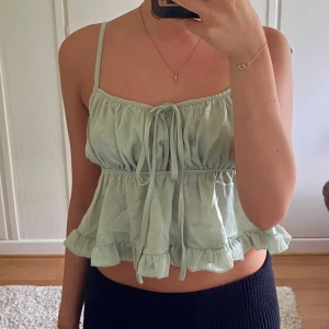 Ljusgrön volangig linnetopp - Supersöt mintgrön linnetopp med smala axelband, volangkant och knyt framtill. Toppen har en luftig och flowy passform som ger en romantisk vibe, perfekt för varma dagar.