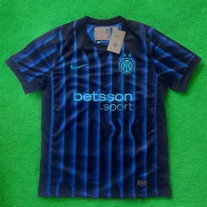 Inter Milan randig matchtröja Nike - Inter Milan fotbollströja i svart och blått med vertikala ränder. Klassisk rund hals, korta ärmar och klubbmärke broderat på bröstet. Nike-logga och sponsortryck i ljusblått. Tillverkad i lätt och ventilerande polyester, perfekt för match eller träning.