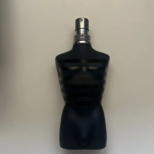 Jean Paul Gaultier Ultra Male parfym - Jean Paul Gaultier Ultra Male parfym i ikonisk svart flaska formad som en manlig torso med matta och blanka ränder. Kommer med original svart cylinderförpackning med röd text och en röd sammetsbas. En maskulin och modern doft med snygg design.