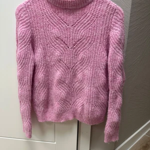 Rosa stickad tröja S - Mysig rosa stickad tröja med snyggt mönster och lång ärm. Tröjan har en högre krage och är perfekt för kyliga dagar. Den stickade strukturen ger en trendig och avslappnad vibe.