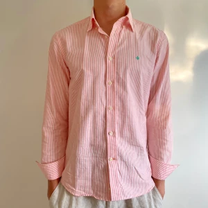 Randig skjorta från Morris - Säljer en klassisk skjorta från Morris i storlek M 39/40 med smala rosa och vita ränder. Skjortan är i riktigt fint skick, inga skavanker. Tillverkad i mjuk bomull och passar perfekt till de varma dagarna!