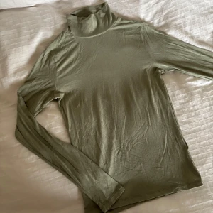 Olivgrön polotröja från Gina Tricot - Säljer en tunn och mjuk olivgrön polotröja från Gina Tricot i storlek S. Tröjan har lång ärm och hög krage, materialet är mjukt och stretchigt