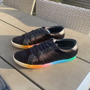 Saint Laurent sneakers - Svarta sneakers från Saint Laurent med snygg regnbågsfärgad sula i orange, rosa, blått och grönt. Skorna har snörning, rund tå och är tillverkade i skinn och textil. Perfekta för dig som vill sticka ut med en färgglad detalj på fötterna.