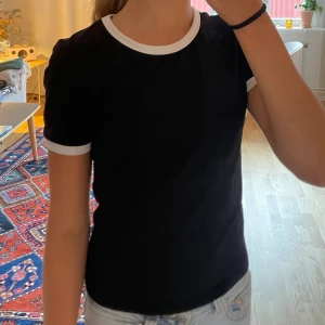 Svart t-shirt med vita kanter Gina Tricot - En svart t-shirt från Gina Tricot i storlek S med vita kontrastkanter vid halsringning och ärmslut. 