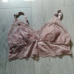 Rosa spetsig linnetopp i spets S - Superfin ljusrosa linnetopp i spets med tunna axelband och vacker blommig spetsdetalj. Toppen har en feminin v-ringning och bred spetskant nedtill. Perfekt att styla under en skjorta eller till höga jeans för en trendig look.