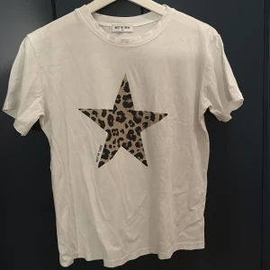 Vit t-shirt med leopardstjärna Meet Me There - Vit t-shirt från Meet Me There med en stor stjärna i leopardmönster på bröstet. Klassisk rund halsringning och korta ärmar. Skön och mjuk bomullskvalitet, perfekt för en cool och avslappnad look.