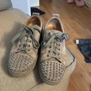 Grå mockasneakers med nitar från Paris - Unika grå sneakers i mocka med coola nitar på tån och breda grå snören. Skorna har rund tå, platt sula och snygga detaljer som ger en edgy vibe. Perfekta för dig som vill sticka ut med din stil och gillar streetwear-inspirerade skor.