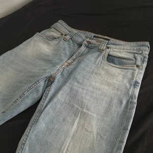 Ljusblå skinny jeans från Nudie - Säljer ett par ljusblå skinny jeans från Nudie Jeans med klassisk femficksdesign. Jeansen har orangea sömmar, läderpatch bak och är tillverkade i mjuk bomullsdenim. Perfekta för dig som gillar en smal passform och stilren look. Tyvärr utan storlek men passar xs/s