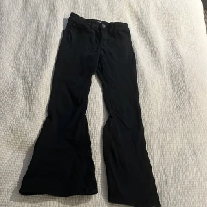 Svarta bootcut byxor från Lindex - Svarta byxor från Lindex med bootcut-modell och klassisk femficksdesign. Byxorna har normal passform och är tillverkade i ett mjukt material som ger en snygg siluett. Perfekta för dig som gillar en retrovibe och vill sticka ut lite extra.