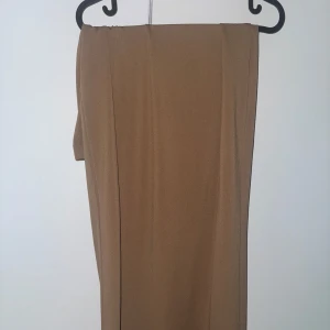 Lång kjol  - Säljer en stilren beige/brun långkjol med rak passform och elastisk midja. Kjolen är enkel och clean utan mönster eller detaljer, perfekt för dig som gillar minimalistisk stil. Materialet känns mjukt och stretchigt, vilket gör den bekväm att bära hela dagen. Storlek L.