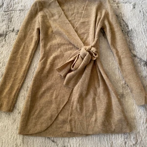 Beige omlottkofta med knytband - Snygg beige omlottkofta med långa ärmar och breda knytband i midjan. Koftan är stickad och har en mjuk känsla. Passar dig som gillar en stilren och mysig look.