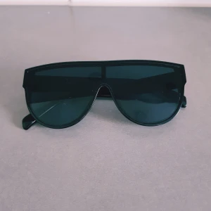 Svarta futuristiska solglasögon - Snygga svarta solglasögon med breda bågar och shield-formade linser. De har en modern, futuristisk vibe och passar perfekt om du vill sticka ut. Tillverkade i blank plast med helsvarta glas och markerad ram.  Helt & fint skick