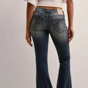 Blå bootcut jeans från True Religion - Snygga blå jeans från True Religion med bootcut-passform och klassiska kontrastsömmar. Jeansen har låg midja, fem fickor och tydliga broderade detaljer! Jeansen är uppsydda i längden till någon sån är ungefär 1,53-1,59