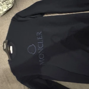 Mörkblå Moncler stickad tröja - Snygg mörkblå stickad tröja från Moncler med broderad logga framtill. Tröjan har rund halsringning och långa ärmar, perfekt för dig som gillar stilrena och exklusiva plagg. Passar dig som vill ha en klassisk look med premiumkänsla.