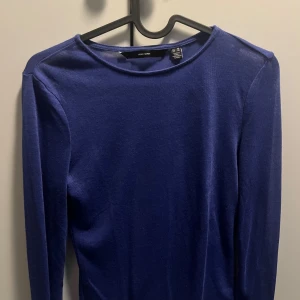 Blå långärmad tröja från Vero Moda - En stilren blå långärmad tröja från Vero Moda. Tröjan har en klassisk rund halsringning och är tillverkad i ett mjukt, tunt material som känns skönt mot huden. Perfekt att styla med jeans eller kjol för en enkel och snygg look.