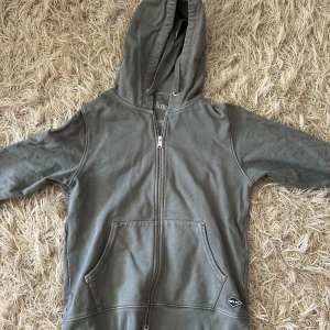 Grå hoodie med dragkedja från Replay - Snygg grön/grå hoodie från Replay med hel dragkedja och huva. Tröjan har känguruficka framtill och en svartvit Replay-logga på fickan. Tillverkad i mjuk bomull, perfekt för chill dagar. Broderad text på insidan av huvan ger extra detalj.