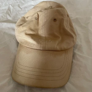 Beige keps från Esprit - Snygg beige keps från Esprit med broderad logga framtill. Klassisk sexpanel-design med böjd skärm och justerbar rem baktill. Tillverkad i bomull för en skön och avslappnad look. Perfekt accessoar för soliga dagar.