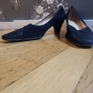 Svarta pumps från Penelope i mocka - Klassiska svarta pumps från Penelope med spetsig tå och låg klack. Skorna är i mocka med detaljer i ormskinnsmönstrad syntet framtill. Perfekta för dig som gillar en tidlös och elegant look.