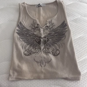  linnetopp med vingar - Säljer en  linnetopp från FB Sister i storlek S. Toppen har ett snyggt tryck med hjärta och vingar framtill, dekorerad med små nitar. Croppad modell med liten v-ringning. Perfekt för dig som gillar edgy detaljer!