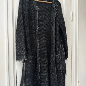 Svart stickad cardigan jacka från Zara - Svart stickad cardigan jacka från Zara med råa kanter och bälte i midjan. Långärmad modell med två stora fickor framtill och en grovstickad struktur som ger en cool och avslappnad vibe. Perfekt för lager-på-lager och chill dagar.