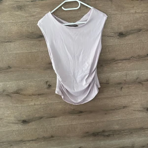 Ljuslila omlottopp från Gina Tricot - Supersnygg ljuslila omlottopp från Gina Tricot i mjuk och stretchig polyester. Toppen är ärmlös med cool öppen rygg och twistad detalj upptill. Perfekt för dig som vill sticka ut med en trendig och unik look.