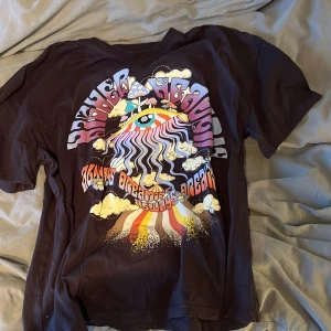 Svart t-shirt med psykedeliskt tryck Bershka - Svart t-shirt från Bershka med färgstarkt psykedeliskt tryck framtill. Trycket har ett stort öga, moln, regnbågsfärger och texten 'Higher Headspace'. Klassisk passform och rund hals. Perfekt för dig som gillar unika statement-plagg.