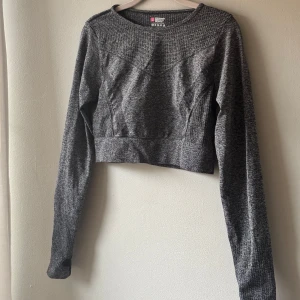 Grå croppad träningströja L - Croppad träningströja i storlek L. Tröjan har lång ärm med tumhål. Figurnära.