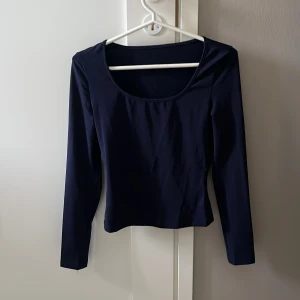 Mörkblå långärmad topp - En stilren mörkblå topp med lång ärm och rundad, djup urringning. Snygg och enkel modell som passar till många olika outfits. Tunt och mjukt material som känns skönt mot huden. Perfekt för dig som gillar minimalistisk stil.HELT NY