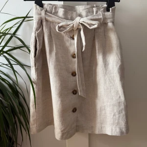 Beige linnekjol  - Säljer en fin beige linnekjol från H&M. Kjolen har knappar framtill, knytskärp i midjan och fickor. Endast använd ett fåtal gånger!