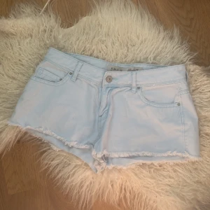 Ljusblå jeansshorts från Denim Co. - Snygga ljusblå jeansshorts från Denim Co. med fransig kant nertill och klassisk femficksdesign. De har låg midja och är perfekta för varma dagar. Materialet är mjukt denim och shortsen har bälteshällor och knappstängning framtill.