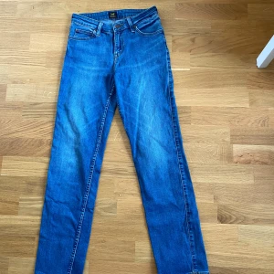 Blå Lee jeans straight fit - Snygga blå jeans från Lee med klassisk femficksdesign och raka ben. Jeansen har normal passform och är tillverkade i slitstarkt bomullsjeans. Perfekta för dig som gillar en tidlös look med enkel Lee-logga på bakfickan. W27 L31.