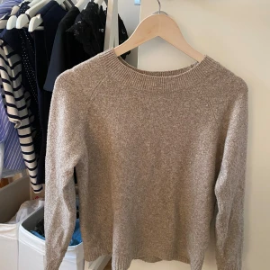 Beige stickad tröja med rund hals - Mysig beige stickad tröja med rundad halsringning och långa ärmar. Perfekt för lager-på-lager och passar till både jeans och kjol. Tröjan har en enkel, klassisk design med ribbade muddar vid ärmslut och nederkant.