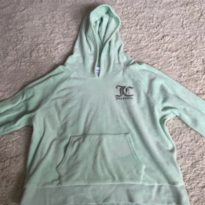 Mintgrön Juicy Couture hoodie  - Supermjuk mintgrön hoodie från Juicy Couture med stor logga på ryggen och mindre logga fram. Klassisk känguruficka och huva. Perfekt för dig som gillar comfy och trendigt med en touch av Y2K-vibe. Storleken är 15/16