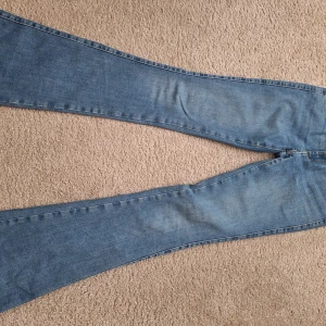 Blå bootcut jeans i storlek S - Säljer ett par ljusblå bootcut jeans i storlek S. Klassisk femficksmodell med dragkedja och knapp framtill. Jeansen har en snygg utsvängd passform och är tillverkade i mjukt denimtyg. Perfekta för dig som gillar retrovibbar och avslappnad stil.