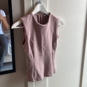 Rosa ärmlös topp från Zara - Supersnygg ljusrosa ärmlös topp från Zara med rund halsringning och figurnära passform. Toppen har en diskret dragkedja i ryggen och är tillverkad i ett mjukt bomullsmaterial. Perfekt att styla med jeans eller kjol för en clean look.