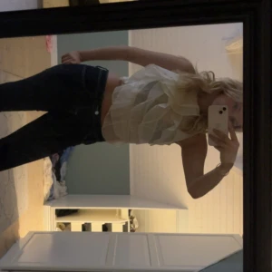 Vit volangig ärmlös blus - Säljer en superfin vit blus med flera lager volanger och ärmlös design. Toppen är lätt transparent och har en luftig känsla, perfekt för att sticka ut. Snygg att styla med jeans eller kjol för en trendig look.