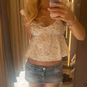 Blommig volangblus med spetsdetaljer - Supersöt blus i ljus bomull med blått blommönster och volangärmar. Toppen har romantiska spetsdetaljer vid axlarna och en luftig, lätt utsvängd passform. Perfekt för dig som gillar en feminin och somrig stil.