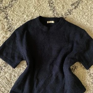 Mörkblå stickad tröja  - Mysig mörkblå stickad tröja med korta ärmar och rund halsringning. Perfekt för lager-på-lager och passar till både jeans och kjol. Enkel och stilren design som funkar året runt.