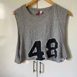 Grå top  - Grå  linnetopp från Divided med stort svart tryck av siffran 48 framtill. Toppen är ärmlös och har en loose passform, perfekt för en avslappnad och sportig look. Tillverkad i mjuk bomull som känns skön mot huden.