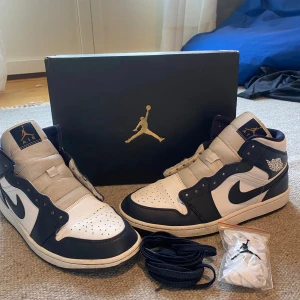 Nike Air Jordan 1 Mid vit/marinblå - Säljer ett par Nike Air Jordan 1 Mid i vit och marinblå färg. Perfekta för dig som vill sticka ut med en ikonisk sneaker.                                     Nypris: 3000kr
