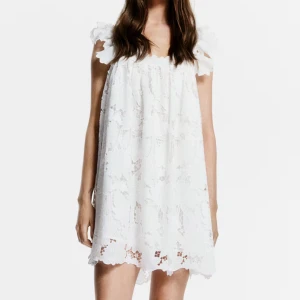 Vit spetsklänning med volangärmar - Superfin vit kort klänning i spets med volangiga axelband och lös passform. Klänningen har blommigt spetsmönster och söt scallop-kant nertill. Från HM x White Lotus kollektion😍