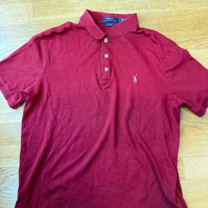Röd pikétröja från Polo Ralph Lauren - Klassisk röd pikétröja från Polo Ralph Lauren i bomull. Tröjan har krage, tre knappar framtill och den ikoniska broderade polospelaren på bröstet. Classic fit för en avslappnad stil, perfekt till jeans eller shorts.