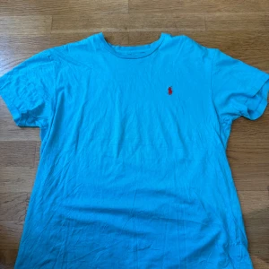Blå t-shirt från Polo Ralph Lauren - Snygg blå t-shirt från Polo Ralph Lauren med klassisk röd broderad logga på bröstet. T-shirten har rund halsringning och är tillverkad i mjuk bomull. Perfekt för en chill och stilren look.