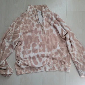 Beige leopardmönstrad tröja Stories - Säljer en beige och vit leopardmönstrad tröja från Stories i storlek L. Tröjan har lång ärm, hög krage och en snygg half zip-dragkedja med ringdetalj. Perfekt för dig som gillar djurmönster och vill ha en chill men trendig look.