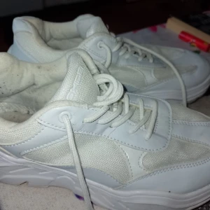 Vita chunky sneakers från Oxide - Säljer ett par vita chunky sneakers från Oxide med cool retrovibe. Skorna har en blandning av syntet och mesh, snörning och en rejäl platt sula. Perfekta för dig som gillar streetstyle och vill ha en clean look.