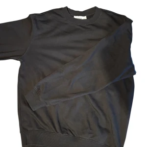 Svart sweatshirt från Weekday - En stilren svart sweatshirt från Weekday med rund halsringning och långa ärmar. Tröjan är i mjuk bomull och har ribbade muddar vid ärmslut och nederkant. Perfekt för en clean och avslappnad look.