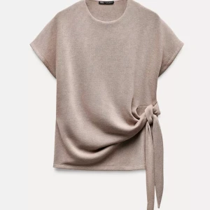 Beige topp med knyt från Zara - Superfin beige topp från Zara med korta ärmar och snygg knytning i sidan. Mjuk och skön i bomullsmix, perfekt till jeans eller kjol. Enkel och stilren design.