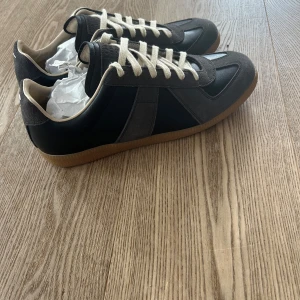 Svart och grå/bruna maison margiela gats i skinn och mocka - Säljer dessa helt nya maison margielas för ett kanon pris i storlek 43. För dig som vill ha ett par riktigt fräsha sneakers till skol starten!