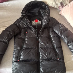 Svart pufferjacka från Zavetti Canada - Snygg svart pufferjacka från Zavetti Canada med stor huva och logga på ärmen. Jackan har blanka paneler, två dragkedjefickor framtill och coolt tryck på huvan. Perfekt för kalla dagar när du vill hålla stilen. Xs men passar S också. Pris kan diskuteras.